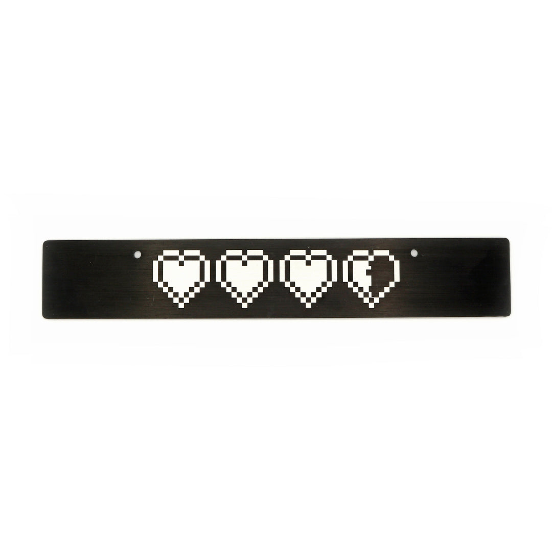 A black anodized aluminum front license plate delete with a pattern of white hearts in a row centered on the plate.
