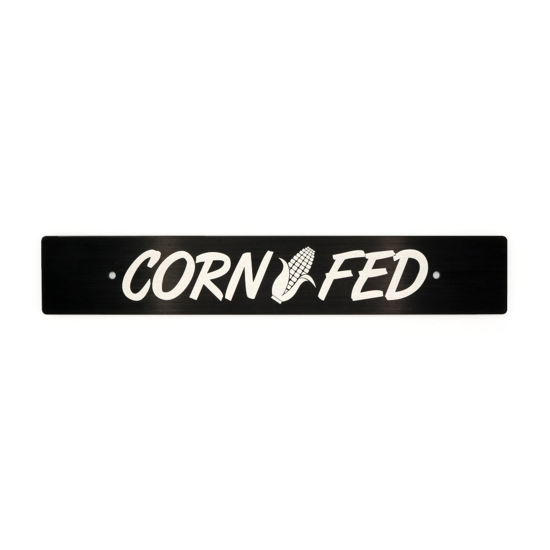 A black anodized aluminum license plate delete with the text 'CORN FED' cut out in the center.