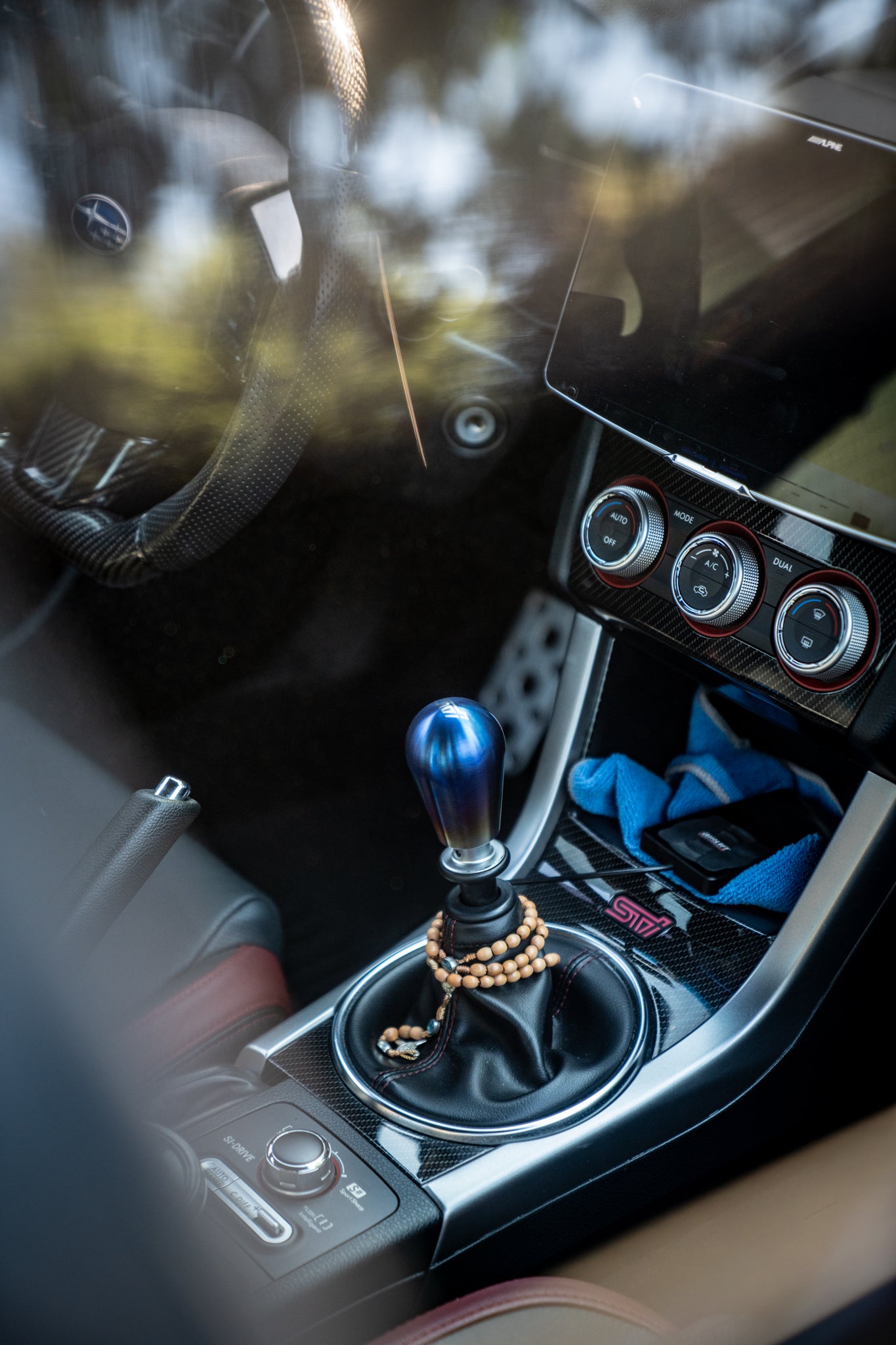Close-up of a car's gear shift lever with a titanium shift knob and decorative chain.