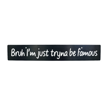 A black anodized aluminum license plate delete with white text that reads 'Bruh I'm just tryna be famous'.