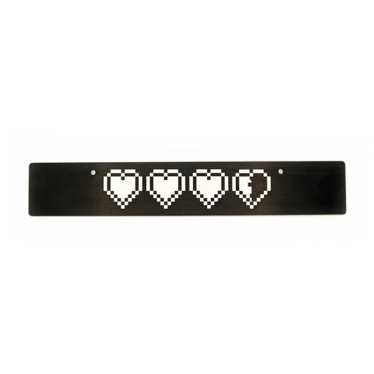 A black anodized aluminum front license plate delete with a pattern of white hearts in a row centered on the plate.