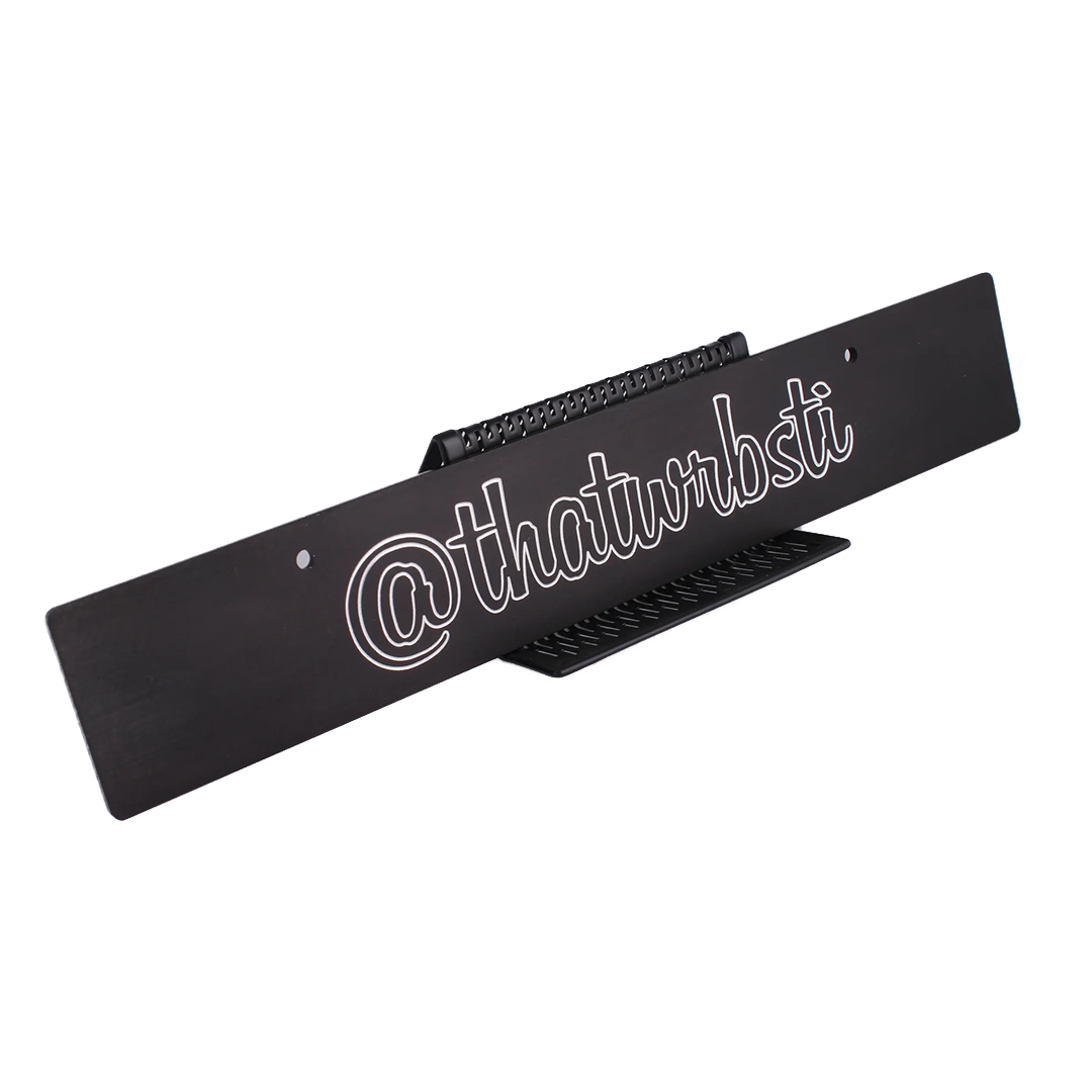 Custom license plate delete with Instagram handle engraved in white, mounted on a black surface.