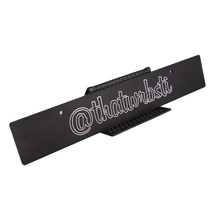 Custom license plate delete with Instagram handle engraved in white, mounted on a black surface.