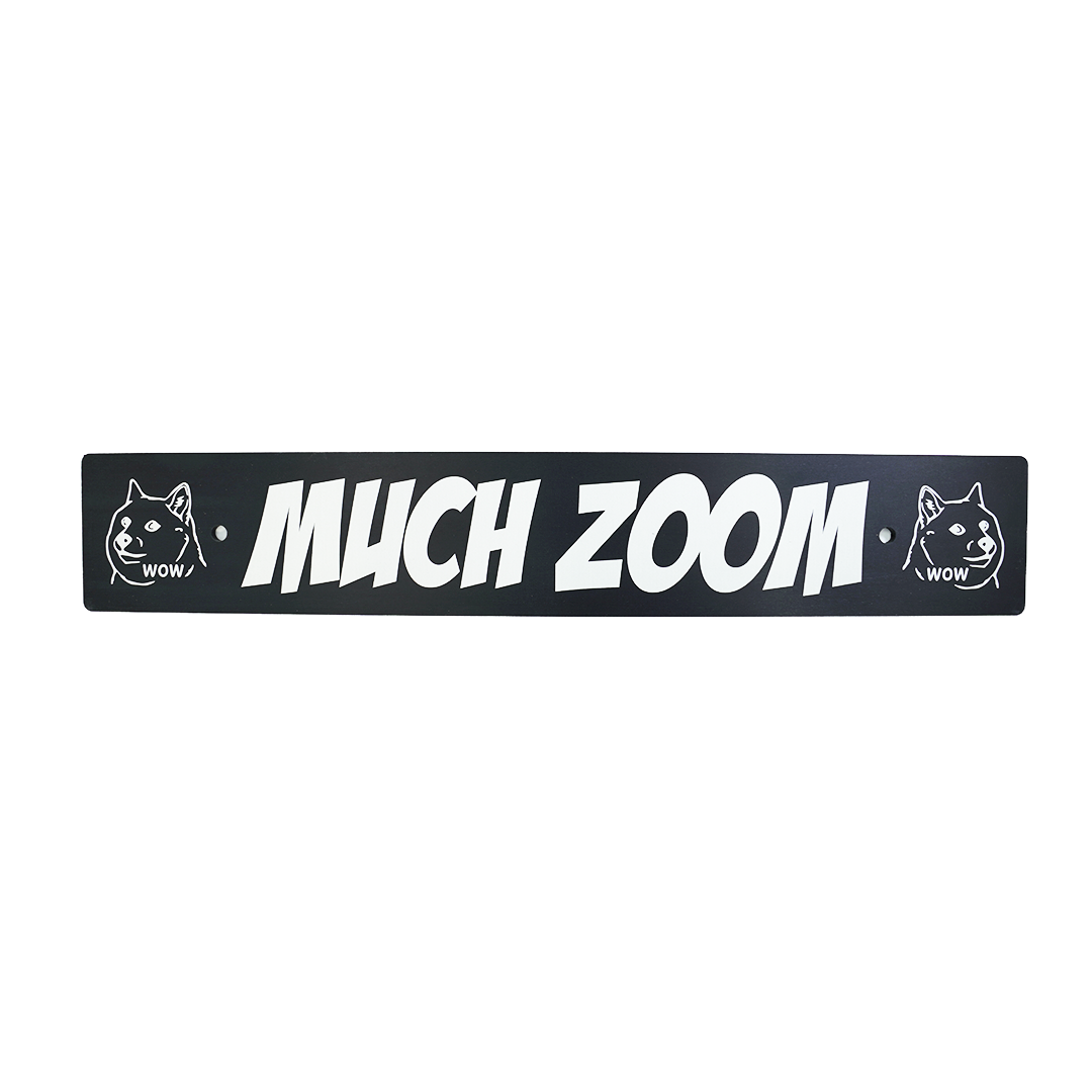 A black anodized aluminum license plate delete with the text 'MUCH ZOOM' in white, along with two cartoon images of Doge on the ends.