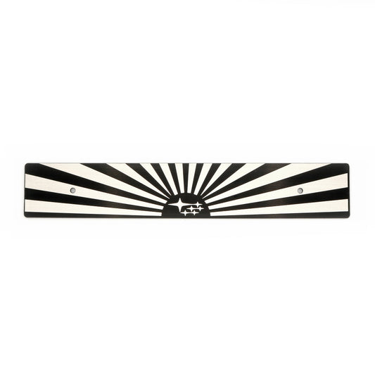 A black and white sun and subaru starburst-patterned license plate delete with mounting holes.