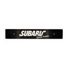 A black anodized aluminum plate with the Subaru logo and the text 'Drive Fresh' on it, intended for use as a front license plate delete.