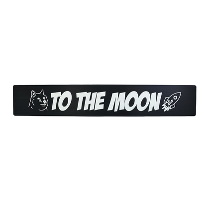 A black anodized aluminum front license plate delete with 'TO THE MOON' text and a rocket illustration in white.