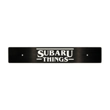 A black front license plate delete with the white text 'Subaru Things' centered on it.